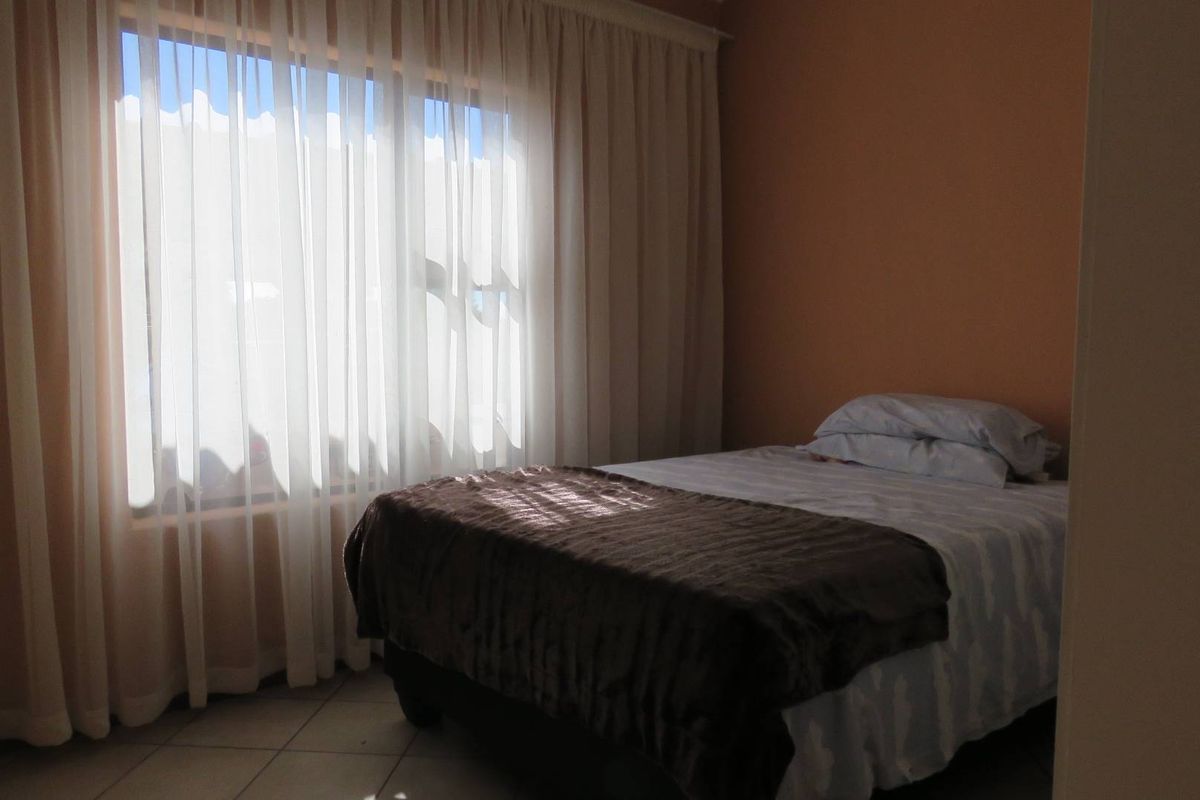 A bedroom featuring tiled flooring and large windows dressed with floor-to-ceiling curtains, providing natural light to the space.