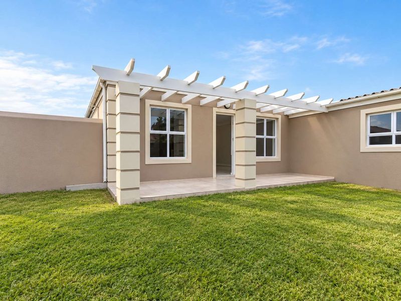 A well-maintained rear patio featuring a white pergola, tiled flooring, and masonry columns, overlooking a neat green lawn.