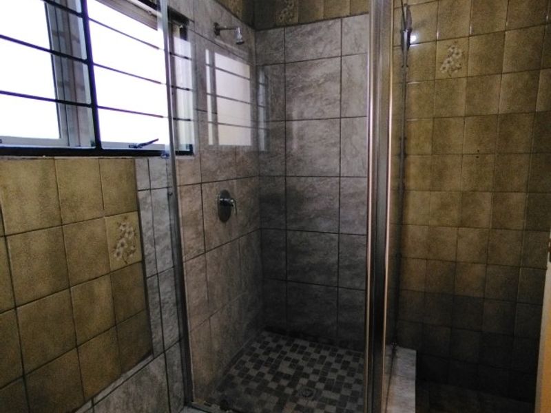 A dated bathroom featuring a glass-enclosed shower with tiled walls and flooring, including a window with security bars.