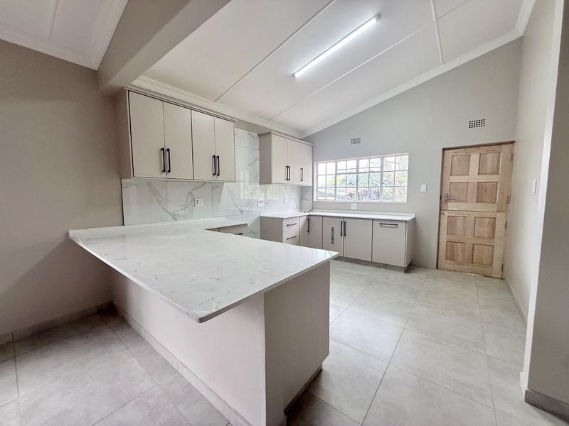 Modern kitchen featuring marble-look quartz countertops, ample built-in cabinetry, tiled flooring, and a clean, neutral aesthetic in an open-plan layout.