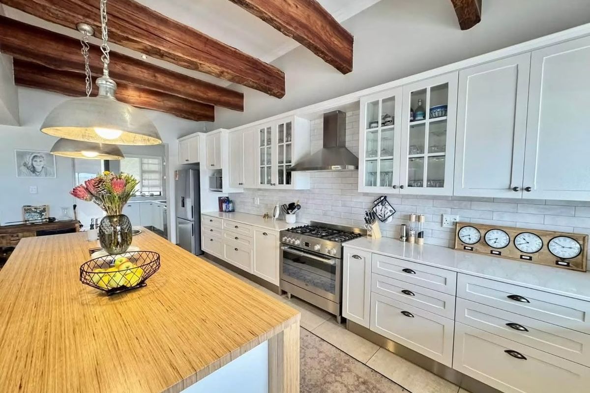 A well-appointed kitchen featuring shaker-style cabinetry, stone countertops, a large island, stainless steel appliances, and rustic exposed timber ceiling beams.