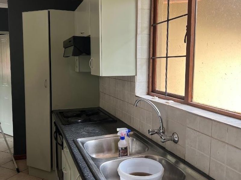 A functional kitchen featuring built-in cabinetry, a double stainless steel sink, integrated hob and oven, and tiled backsplash with a window view.
