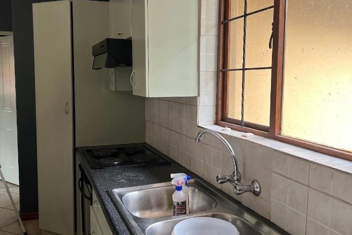 A functional kitchen featuring built-in cabinetry, a double stainless steel sink, integrated hob and oven, and tiled backsplash with a window view.