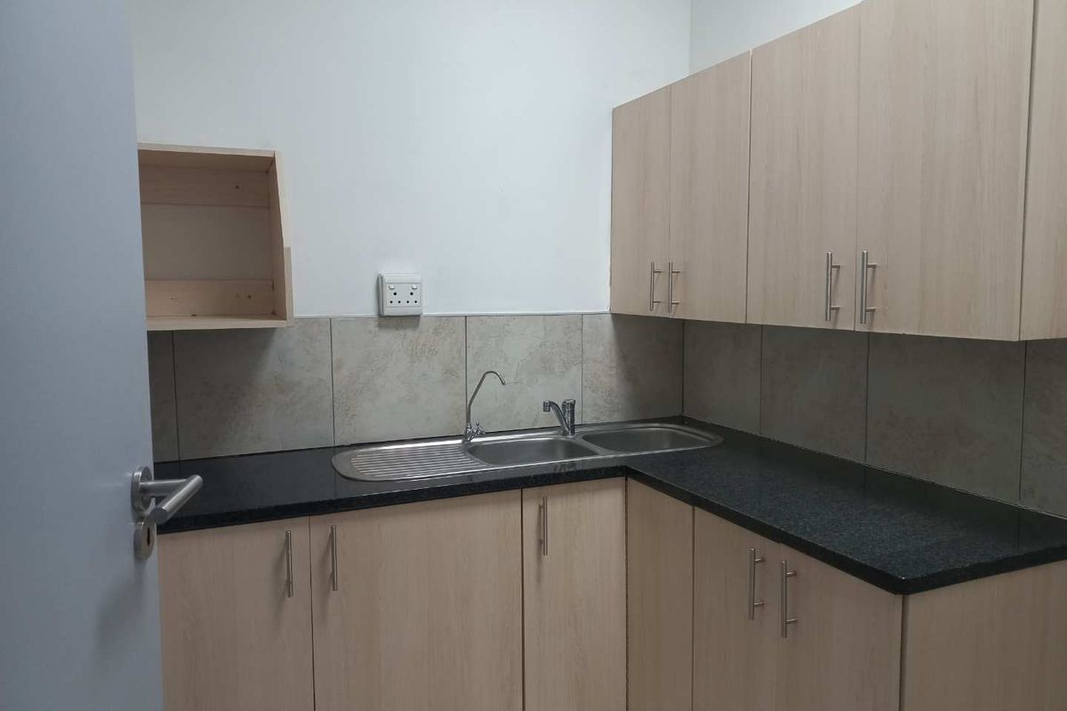 A functional office kitchenette featuring light wood-finish cabinetry, dark granite-look countertops, a stainless steel sink, and tiled splashbacks.