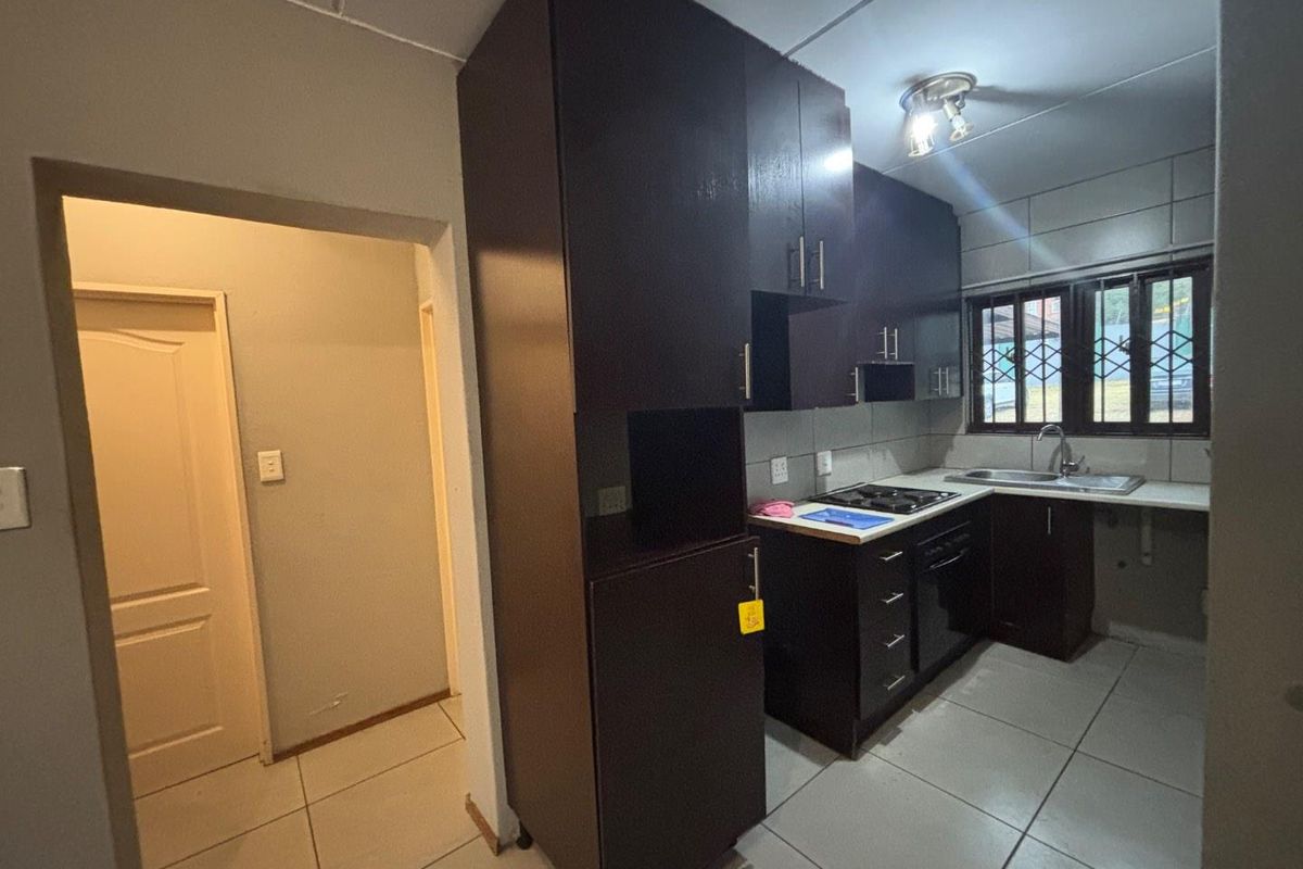 Compact kitchen featuring dark built-in cabinetry, a built-in oven and hob, stainless steel sink, and tiled flooring.