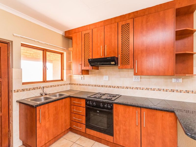A functional kitchen featuring wooden cabinetry, granite countertops, a built-in oven with hob, and a tiled backsplash.