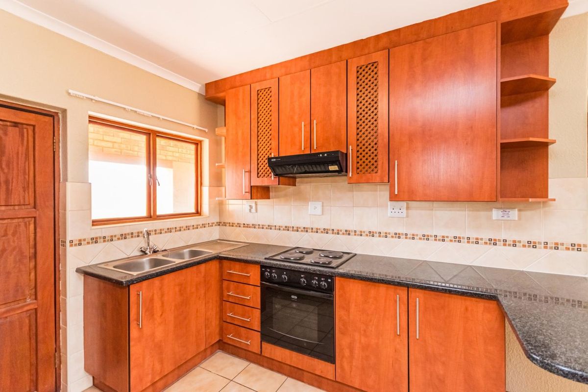 A functional kitchen featuring wooden cabinetry, granite countertops, a built-in oven with hob, and a tiled backsplash.