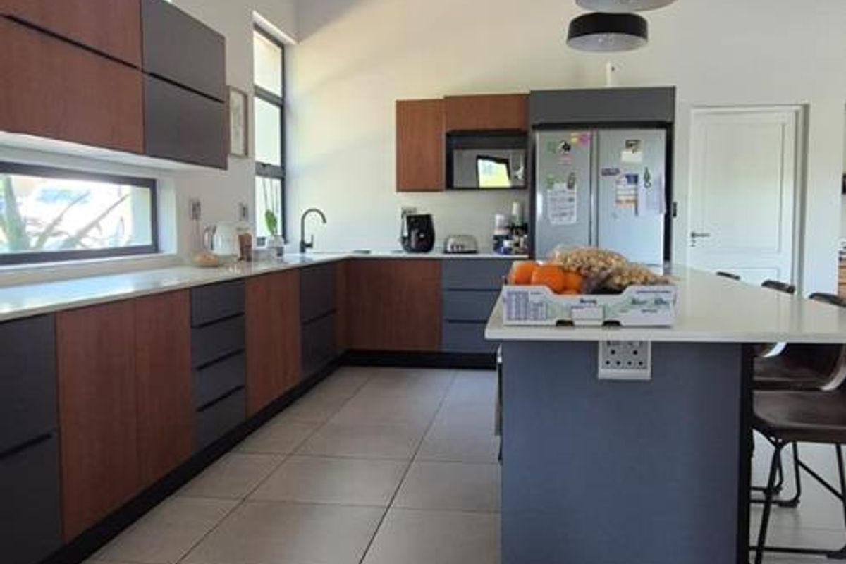 Modern kitchen featuring two-tone cabinetry, a central island with breakfast bar seating, tiled flooring, and high vaulted ceilings with exposed beams.