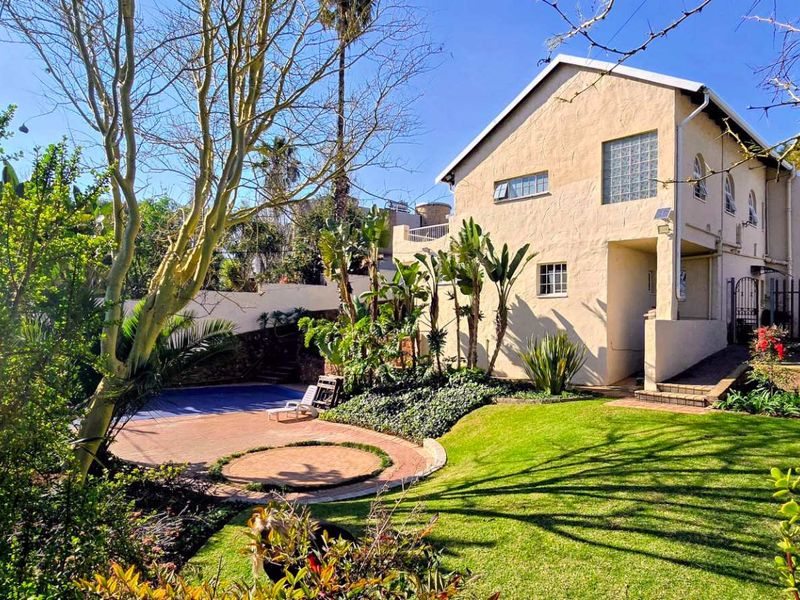 Rear view of the property featuring a landscaped garden, paved patio area, and a swimming pool set against the building's exterior facade.