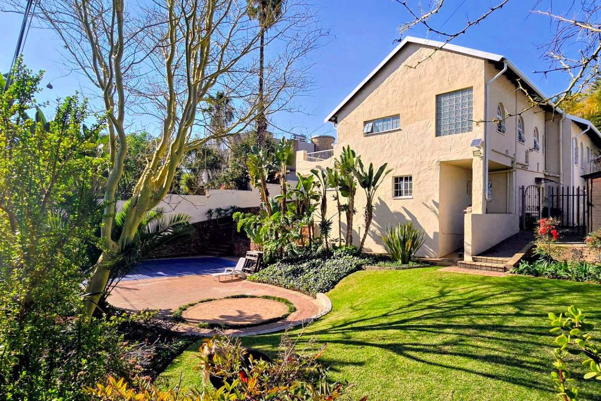 Rear view of the property featuring a landscaped garden, paved patio area, and a swimming pool set against the building's exterior facade.