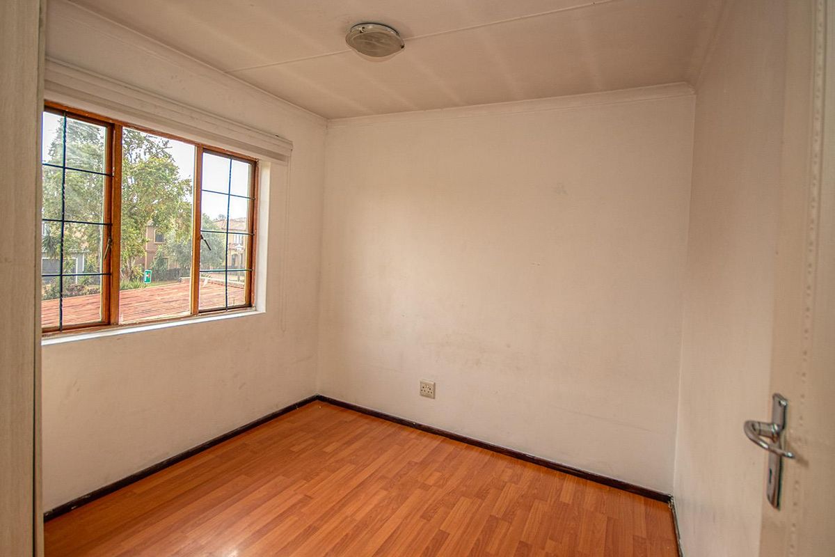 A vacant bedroom featuring laminate wood flooring, a large window with security bars, and a central ceiling light fixture.