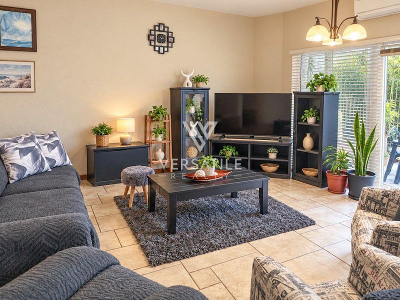 A comfortable living room featuring tiled flooring, an air conditioning unit, and large sliding glass doors that provide access to the outdoor area.