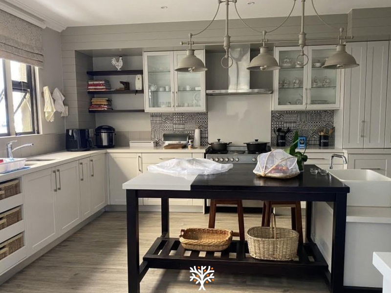 A well-appointed kitchen featuring shaker-style cabinetry, a central island, apron-front sink, gas stove with extractor, and stylish patterned tile backsplash.