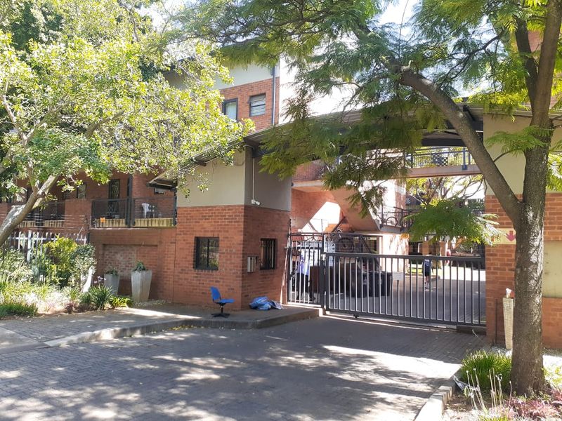 Front entrance view of the apartment complex featuring a brick facade, secure gated access, and paved driveway area.