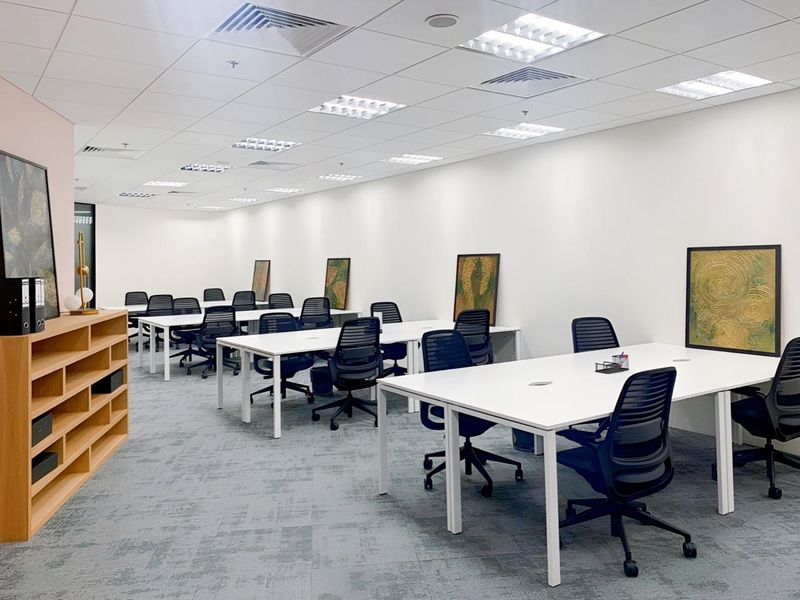 A modern, well-lit open-plan office space featuring a suspended ceiling with integrated lighting, air conditioning vents, and professional carpeted flooring.
