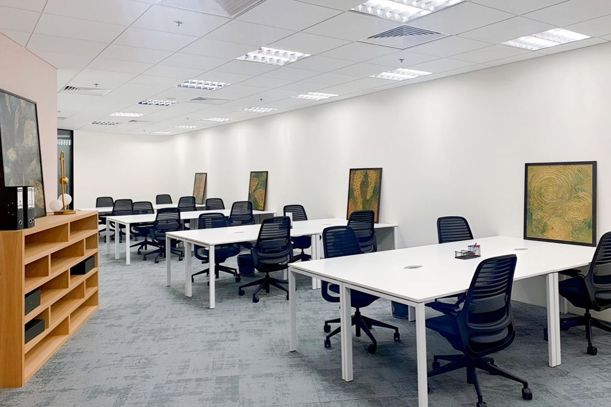 A modern, well-lit open-plan office space featuring a suspended ceiling with integrated lighting, air conditioning vents, and professional carpeted flooring.