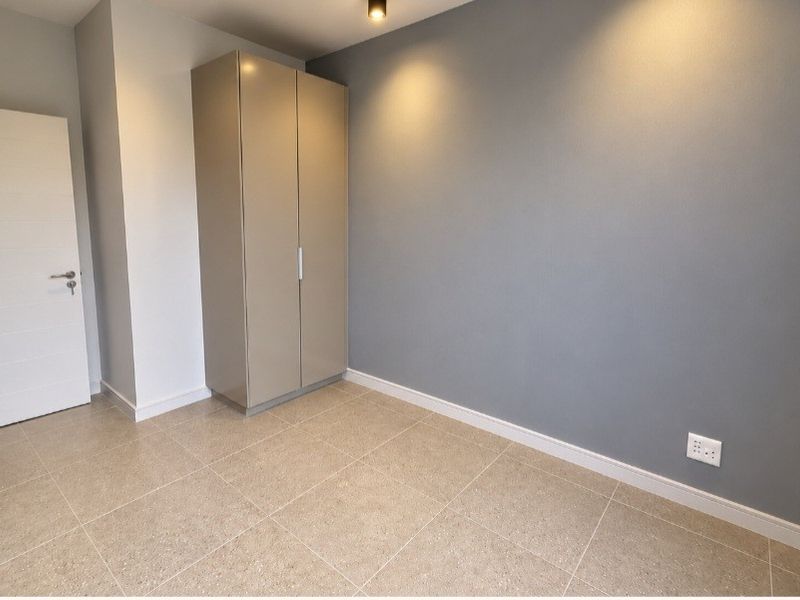 A clean, modern bedroom featuring neutral tiled flooring, a built-in wardrobe, and a contemporary grey accent wall with recessed lighting.