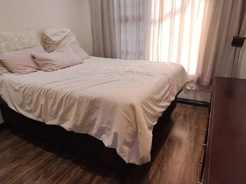 A compact bedroom featuring laminate flooring and large window curtains, providing a functional and private sleeping space.