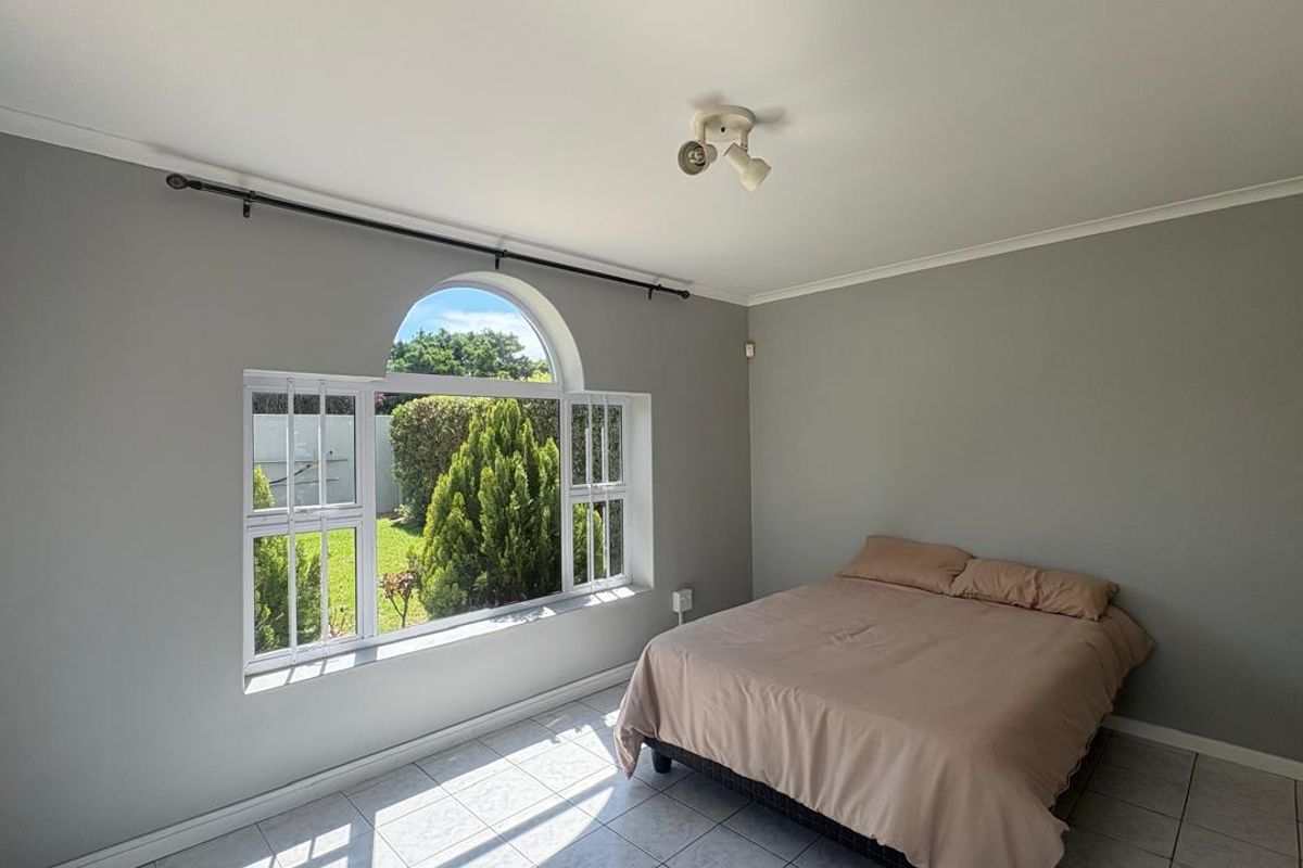 A bright bedroom featuring tiled flooring, a unique arched window with security bars, and neutral grey walls.