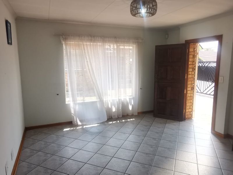 A living room featuring tiled flooring, an intercom system, and a timber entrance door leading to the exterior.