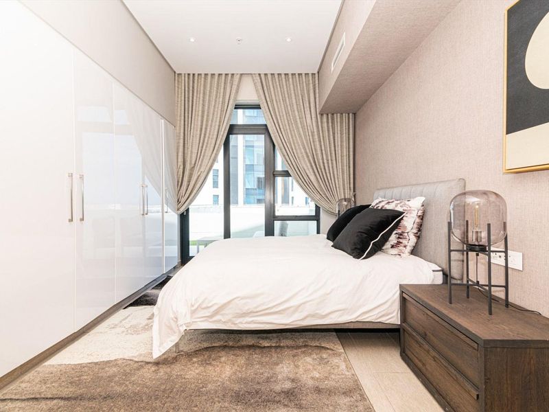 Modern bedroom featuring high-gloss built-in wardrobes, recessed ceiling lighting, and a full-height glass door leading to an outdoor area.