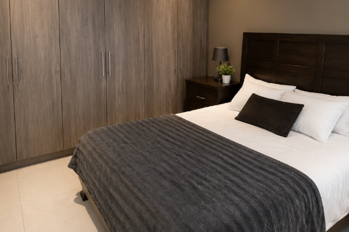 A well-maintained bedroom featuring built-in floor-to-ceiling wooden cabinetry and neutral tiled flooring.