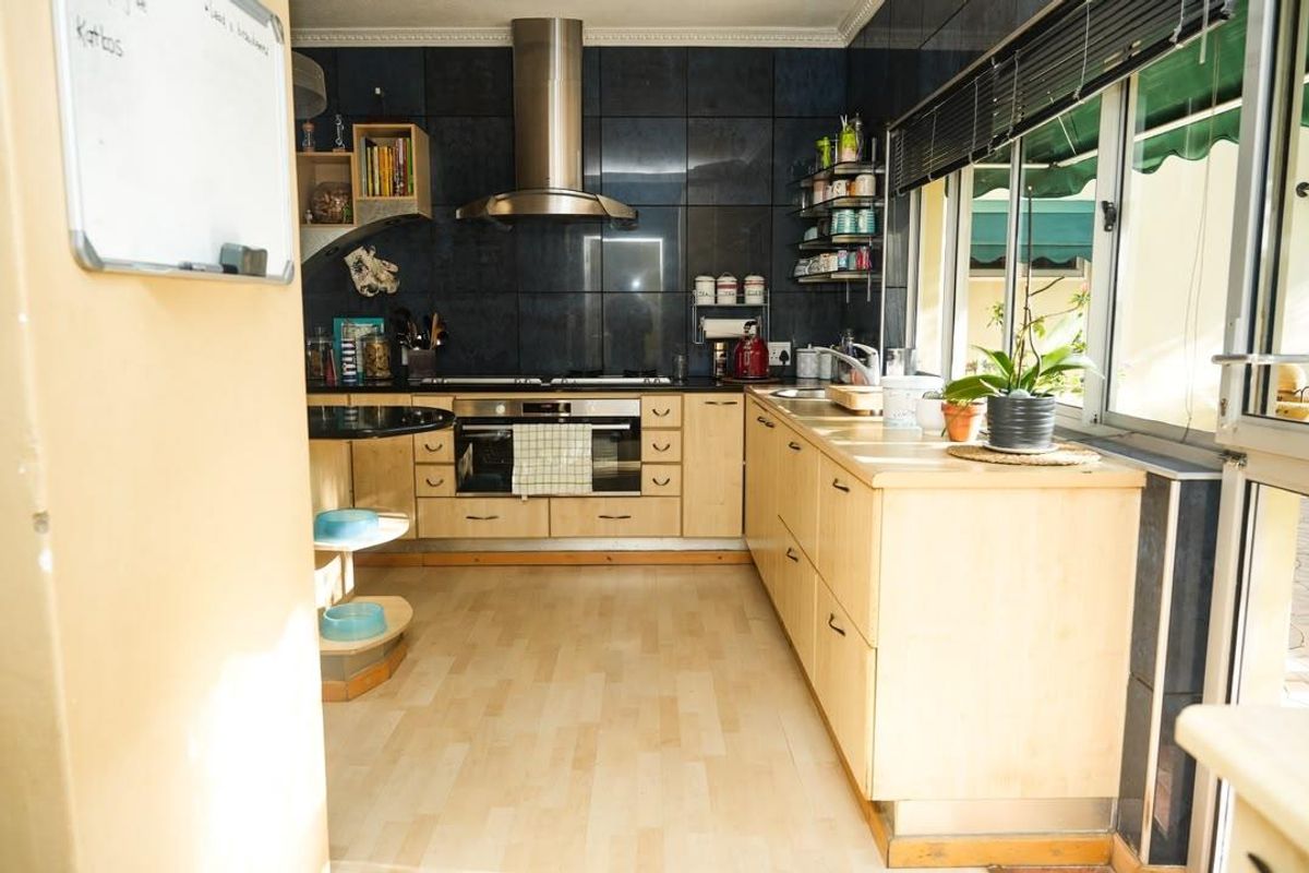 A functional kitchen featuring light wood cabinetry, a stainless steel extractor fan, built-in oven, and dark tiled splashbacks with direct access to an outdoor area.