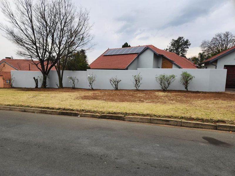 Front view of the property featuring a solid perimeter wall, tiled roof, and installed solar panels, set behind a neat grass verge.
