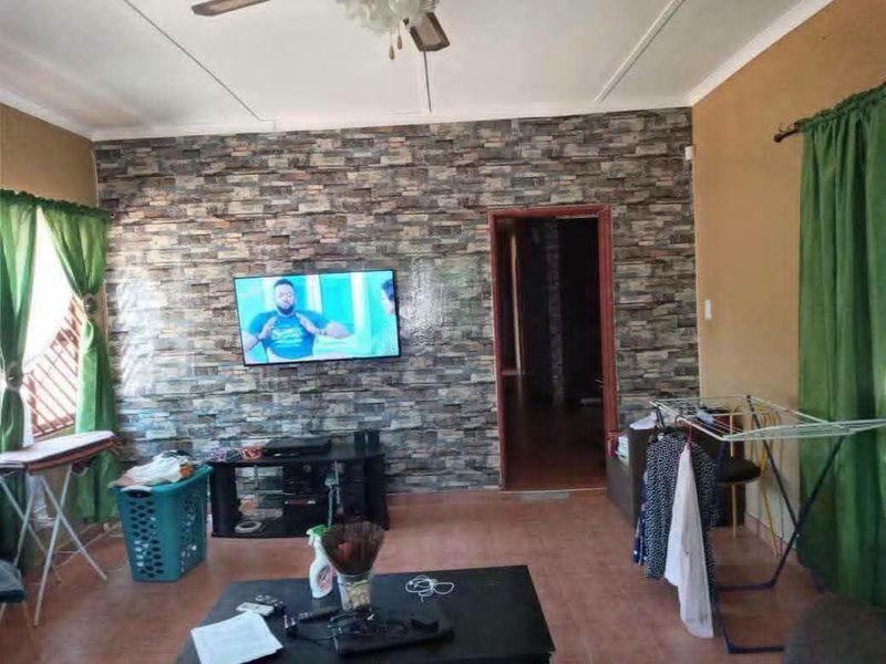 Living room featuring a stone-look accent wall, tiled flooring, and a ceiling fan, offering a functional space with potential for cosmetic updates.