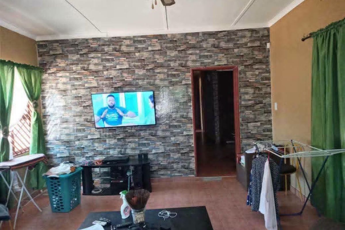 Living room featuring a stone-look accent wall, tiled flooring, and a ceiling fan, offering a functional space with potential for cosmetic updates.