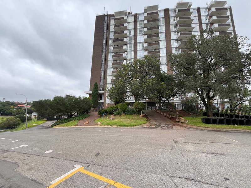 Exterior view of a multi-story apartment building featuring private balconies, a paved driveway, and established garden landscaping.