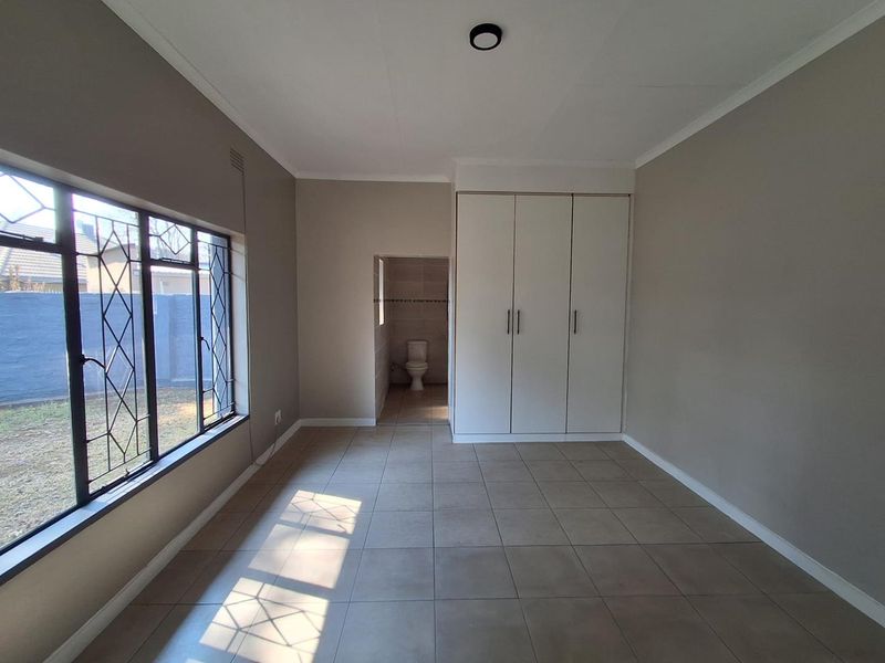 A spacious, empty bedroom featuring neutral tiled flooring, built-in cupboards, and direct access to an en-suite bathroom.
