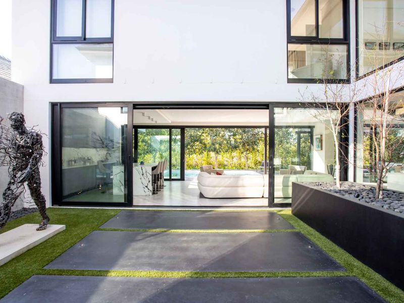 Modern rear courtyard featuring large sliding glass doors, concrete paving, artificial turf, and a raised planter box, seamlessly connecting to the interior living space.