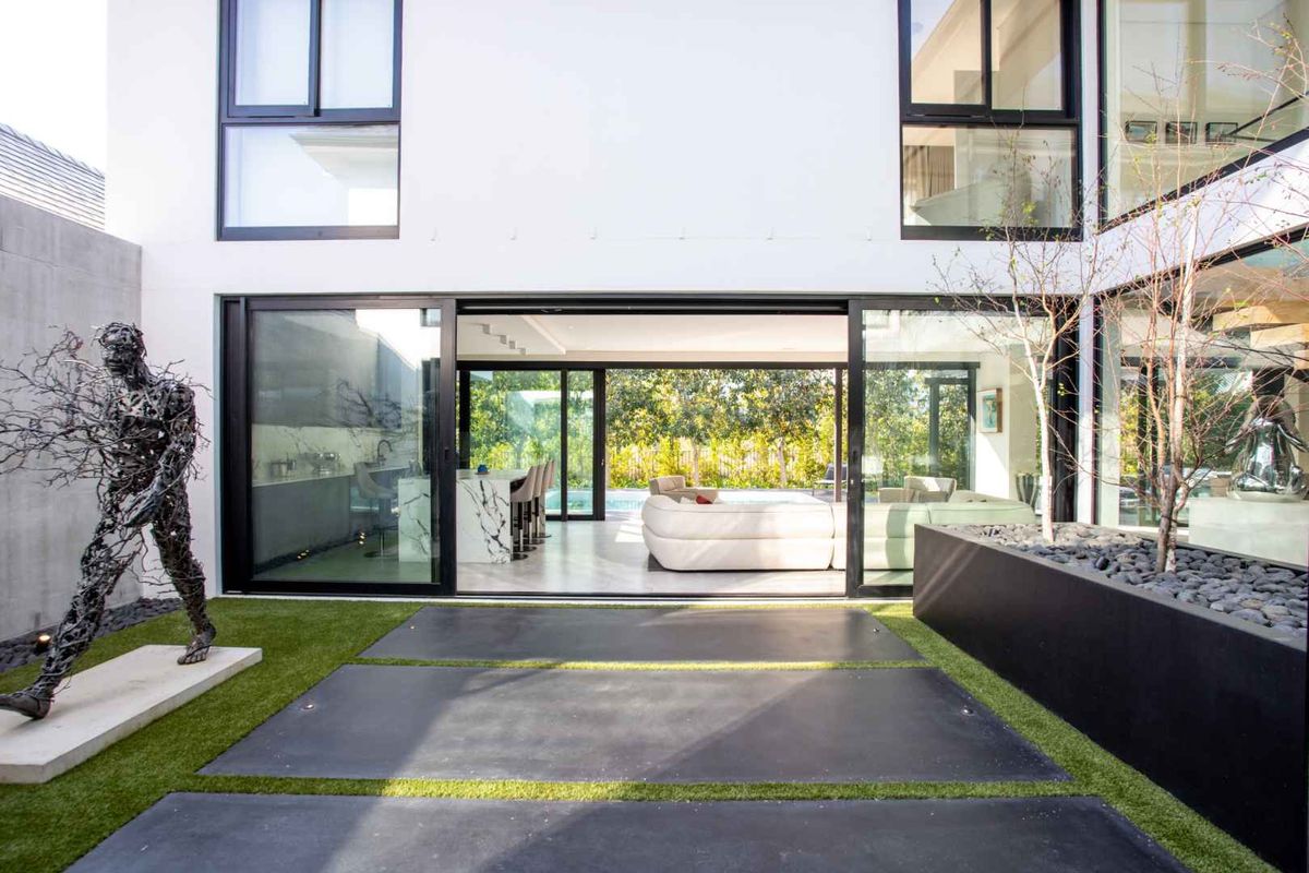Modern rear courtyard featuring large sliding glass doors, concrete paving, artificial turf, and a raised planter box, seamlessly connecting to the interior living space.