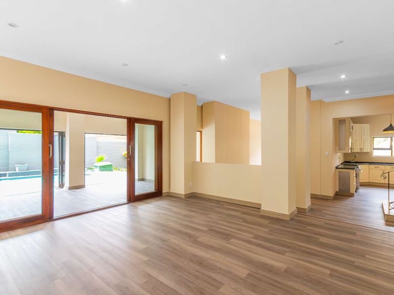 Spacious open-plan living area featuring modern laminate flooring, recessed lighting, and large sliding doors providing seamless access to the outdoor patio and pool area.