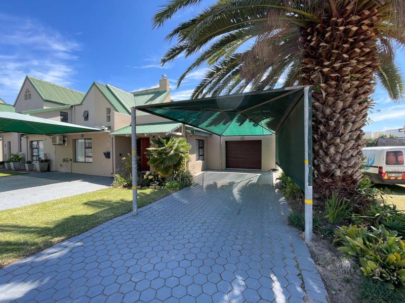 Front exterior view of the house featuring a paved driveway, a shade cloth carport, and a well-maintained garden area.