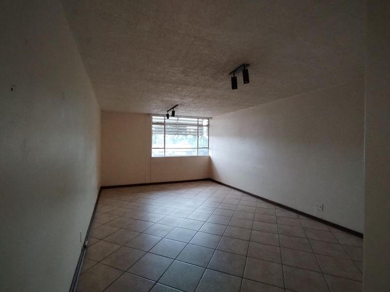 An empty living room featuring tiled flooring, track lighting, and a window with security bars, presenting a blank canvas for renovation.
