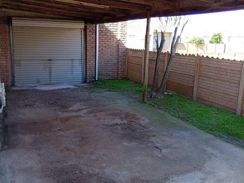 A covered carport area featuring a roller shutter garage door, concrete flooring, and a precast boundary wall.