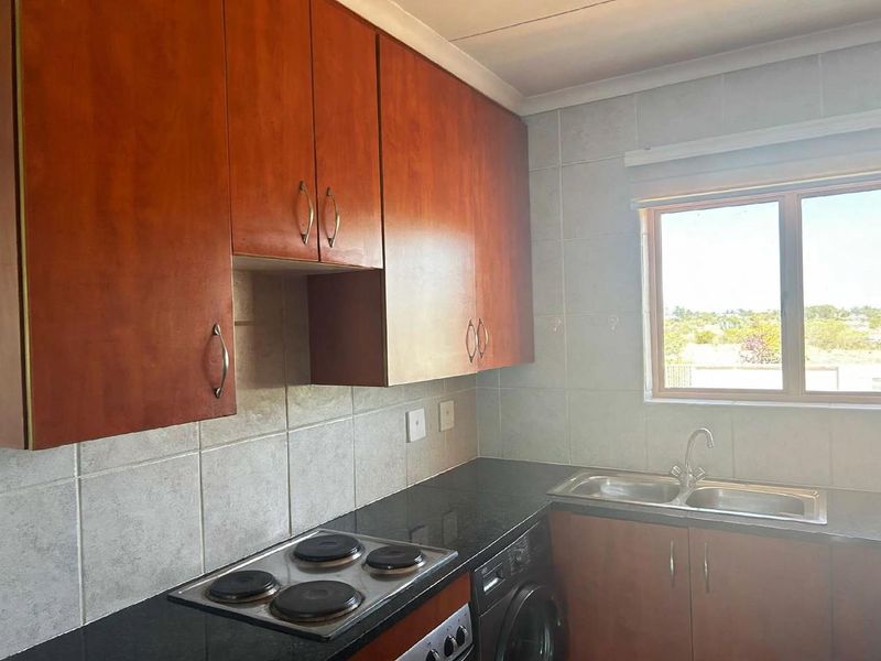 Functional kitchen featuring wood-finish cabinetry, dark countertops, a built-in electric hob, and a stainless steel double sink with tiled splashbacks.