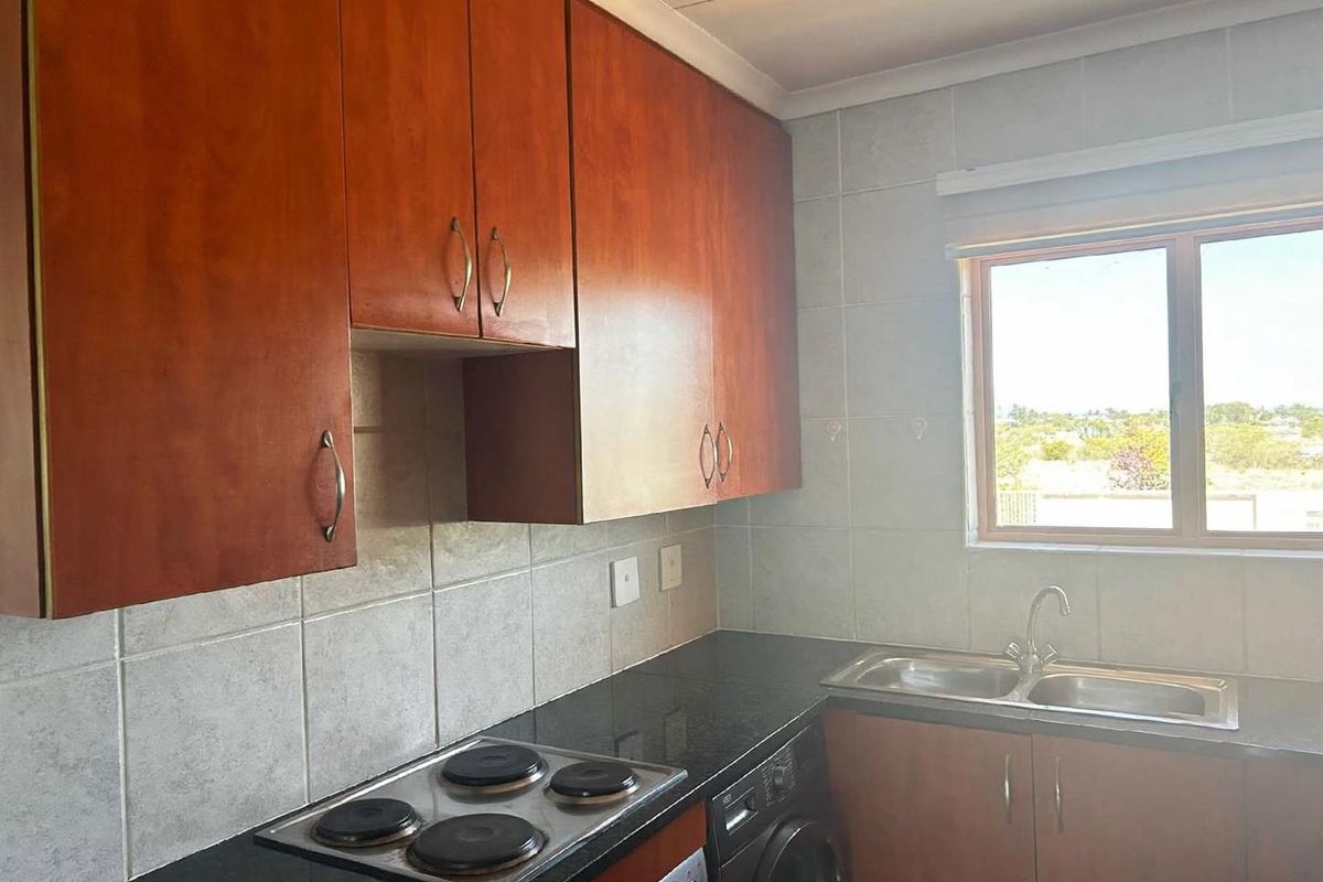 Functional kitchen featuring wood-finish cabinetry, dark countertops, a built-in electric hob, and a stainless steel double sink with tiled splashbacks.