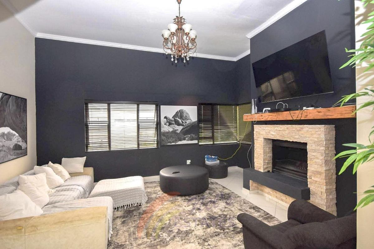 A cozy living room featuring a stone-clad fireplace with a timber mantel, dark accent walls, and large windows with fitted blinds.
