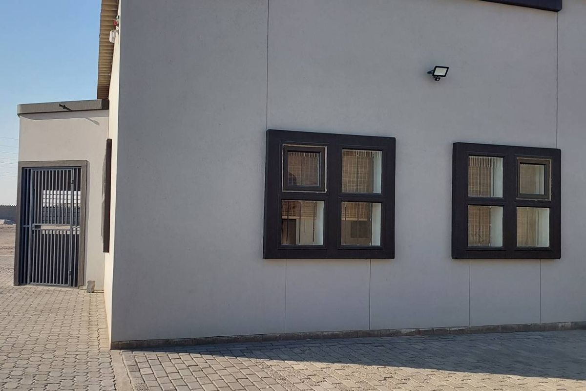 Exterior view of an industrial property featuring a paved driveway, secure gated entrance, and modern facade with framed windows.