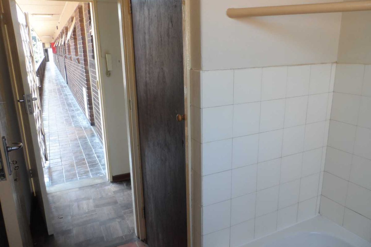 A dated bathroom interior featuring a bathtub with wall tiling, leading out to an external apartment corridor.