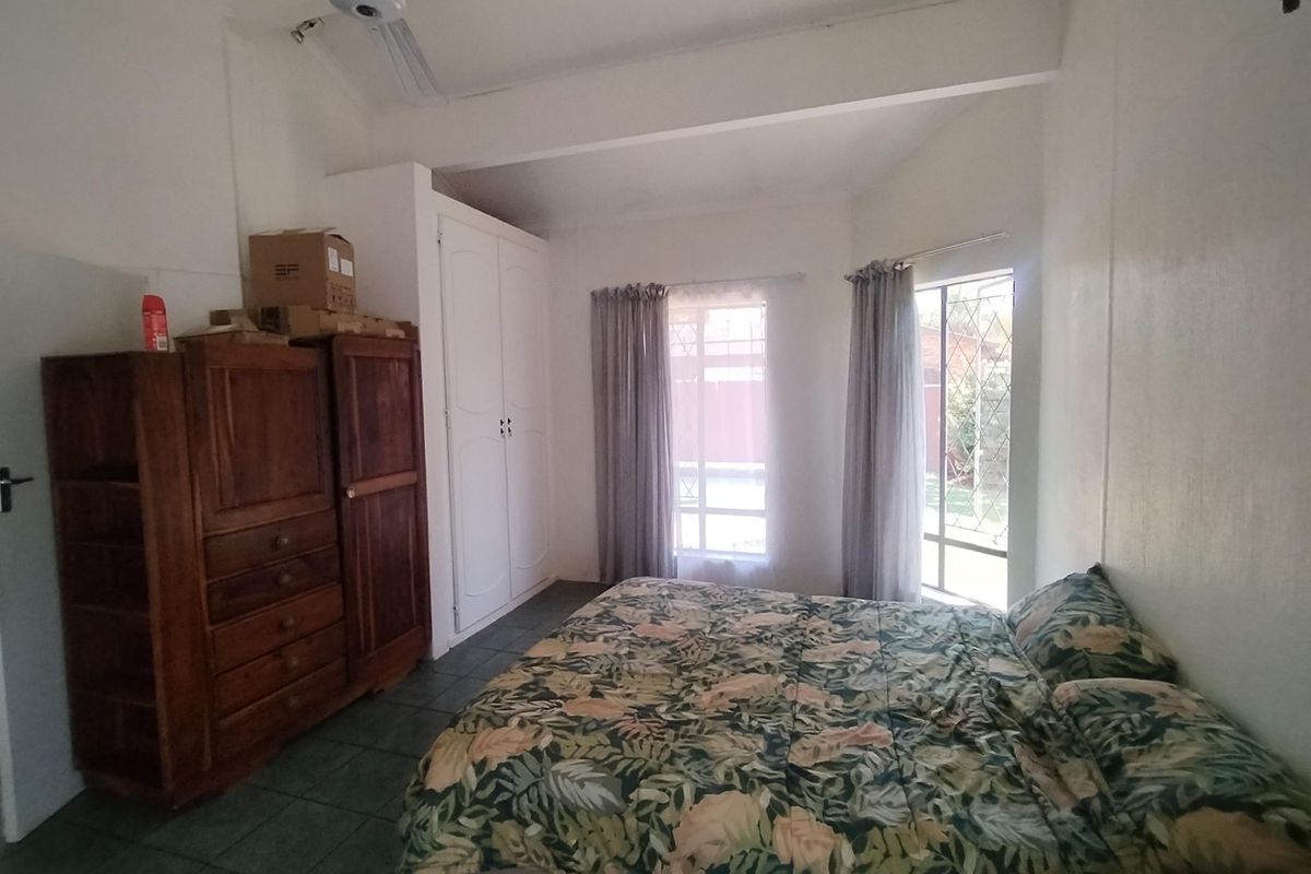 A functional bedroom featuring tiled flooring, a built-in wardrobe, a ceiling fan, and large windows with security bars allowing natural light.