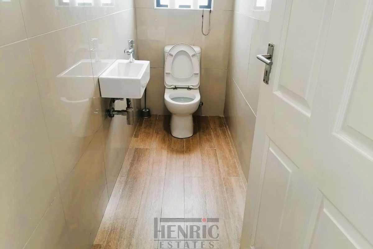 A compact, modern guest bathroom featuring neutral wall tiles, wood-look floor tiles, a wall-mounted basin, and a standard toilet.