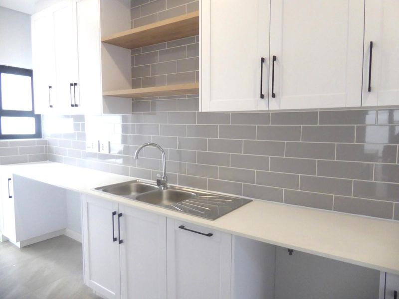 Modern kitchen featuring white shaker cabinetry, grey subway tile backsplash, quartz countertops, and a stainless steel double sink with open wooden shelving.