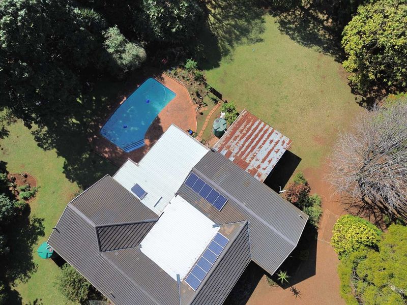 Aerial view of the property featuring a swimming pool, landscaped garden, and a roof equipped with solar panels and sections of weathered metal roofing.