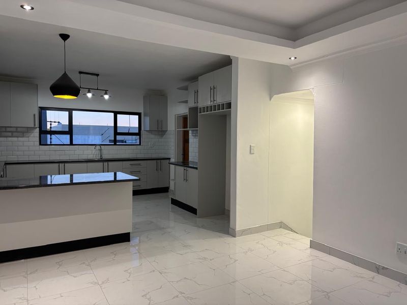 Modern open-plan kitchen featuring sleek cabinetry, granite countertops, subway tile backsplash, and polished marble-look floor tiles in a bright, neutral space.