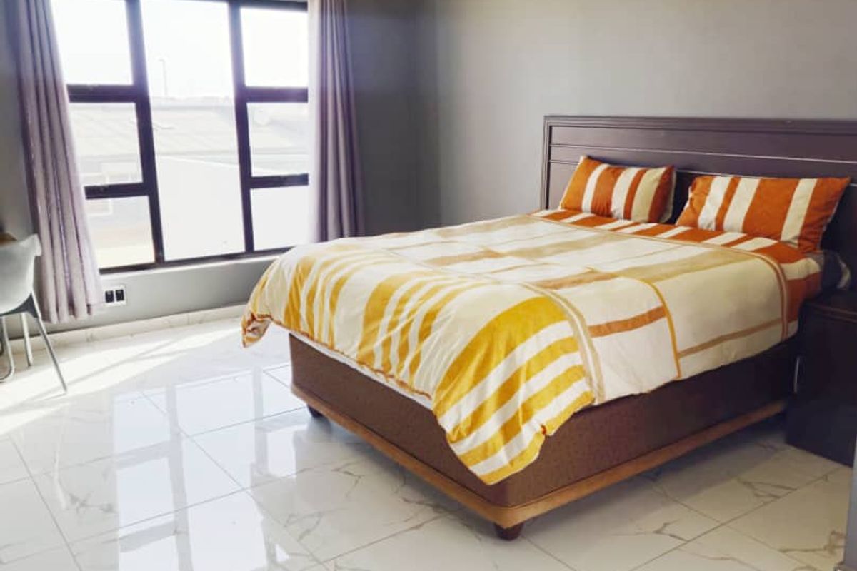 A bright bedroom featuring large windows, modern white marble-look floor tiles, and neutral grey wall finishes.