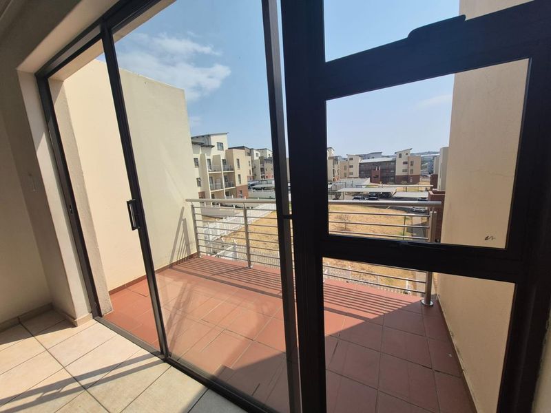 A private balcony featuring tiled flooring and a stainless steel balustrade, offering an open view of the surrounding apartment complex.